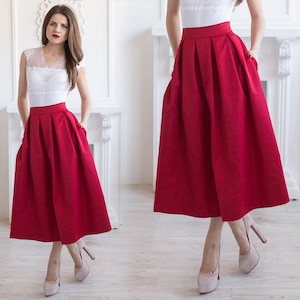 Stylish midi red skirt with a wide pleats. Waist fit, has a sewn-in waistband about two inches wide. Made of polished cotton, with a slight sheen. Pockets in the side seams. Wide cuff at the bottom to keep skirt's shape. Hidden zip at the back.