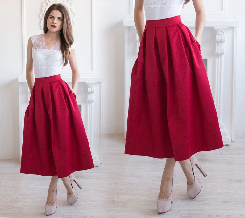 Stylish midi red skirt with a wide pleats. Waist fit, has a sewn-in waistband about two inches wide. Made of polished cotton, with a slight sheen. Pockets in the side seams. Wide cuff at the bottom to keep skirt's shape. Hidden zip at the back.