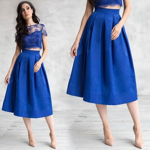 Stylish midi blue skirt with a wide pleats. Waist fit, has a sewn-in waistband about two inches wide. Made of polished cotton, with a slight sheen. Pockets in the side seams. Wide cuff at the bottom to keep skirt's shape. Hidden zip at the back.