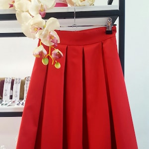 Stylish midi red skirt with a wide pleats. Waist fit, has a sewn-in waistband about two inches wide. Made of polished cotton, with a slight sheen. Pockets in the side seams. Wide cuff at the bottom to keep skirt's shape. Hidden zip at the back.