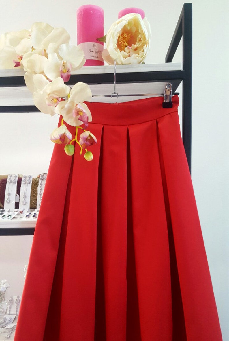 Stylish midi red skirt with a wide pleats. Waist fit, has a sewn-in waistband about two inches wide. Made of polished cotton, with a slight sheen. Pockets in the side seams. Wide cuff at the bottom to keep skirt's shape. Hidden zip at the back.