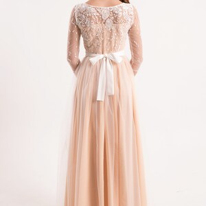 May include: A long, peach-coloured tulle dress with a white lace bodice and a white satin sash tied at the waist.