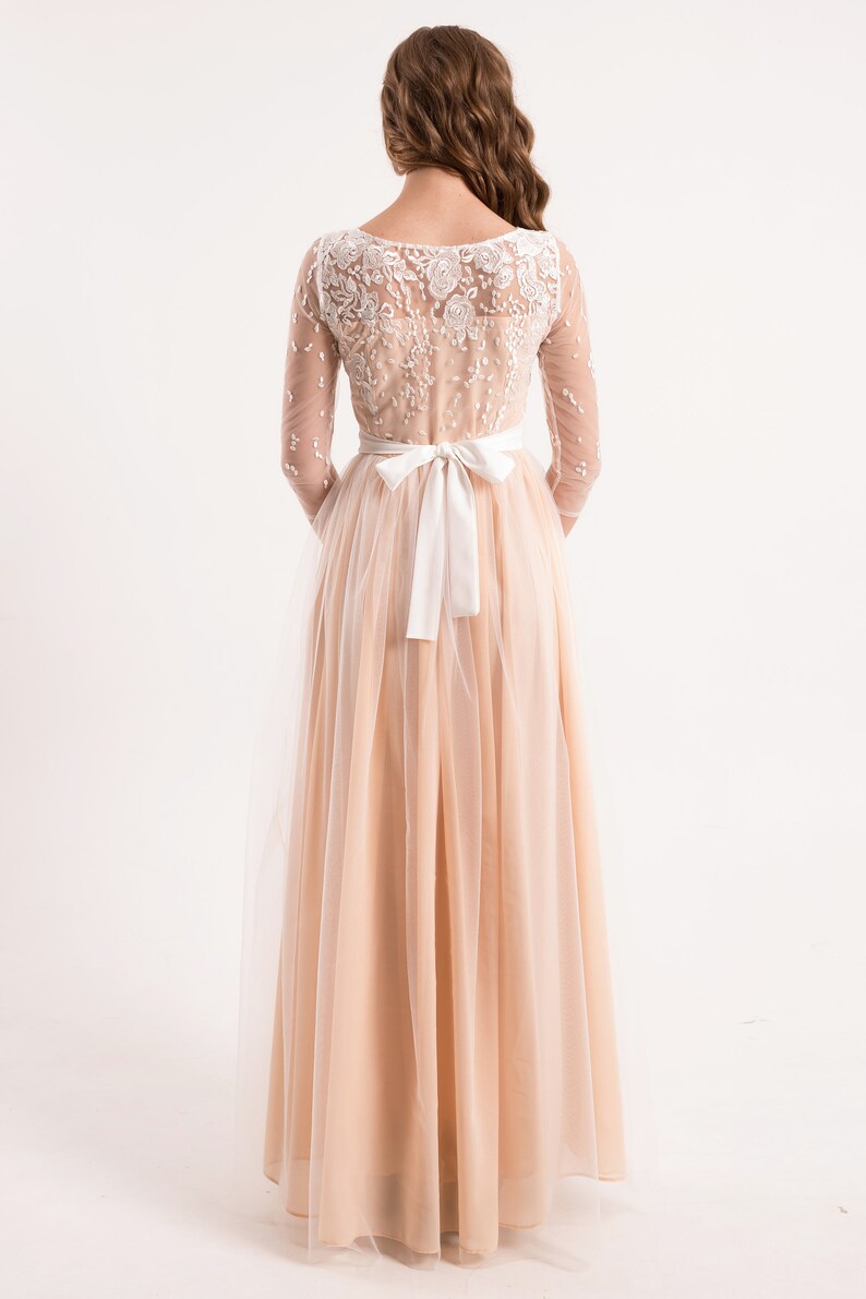 May include: A long, peach-coloured tulle dress with a white lace bodice and a white satin sash tied at the waist.