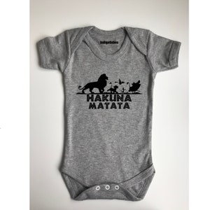 May include: Gray baby onesie with a black silhouette of Simba and other characters from The Lion King. The text "Hakuna Matata" is printed below the image.