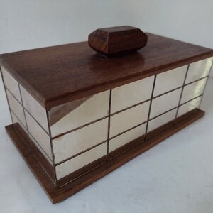 Puede incluir: Una caja de madera con un interior de espejo. La caja tiene una tapa con bisagras y un pomo de madera decorativo en la parte superior. El espejo está dividido en cuadrados pequeños.