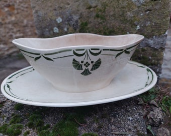 May include: A white ceramic gravy boat with a green floral design and a matching saucer. The boat has a scalloped edge and the saucer has a simple green border.