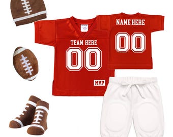 Könnte beinhalten: Ein rotes Baby-Outfit-Set zum Thema Football. Das Set enthält ein Trikot mit dem Text "TEAM HERE" und "MVP", ein passendes Shirt, eine weiße Hose, eine Mütze, einen Football und Socken. Das Trikot und das Shirt haben die Nummer "00".