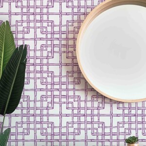 May include: A white wall with a purple geometric pattern wallpaper. A round wooden mirror with a white reflective surface is mounted on the wall. A small potted succulent plant is on a wooden shelf below the mirror.