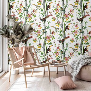 May include: A white wallpaper with a tropical theme featuring toucans, birds, and flowers. The wallpaper is displayed in a room with a wooden chair and a throw pillow.