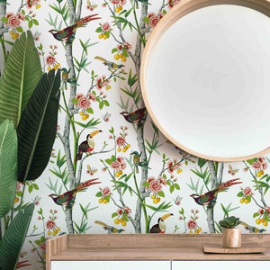 May include: White wallpaper with a repeating pattern of green bamboo branches, pink flowers, yellow fruit, and colourful birds. A round wooden mirror hangs on the wall above a white dresser with two drawers.