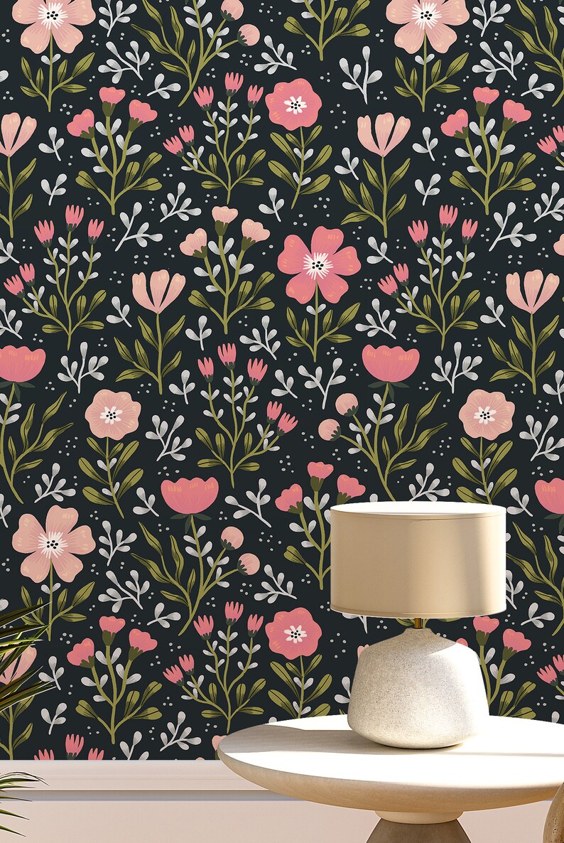 Pu&ograve; includere: Una lampada da tavolo bianca con un paralume beige &egrave; posizionata su un tavolo bianco con uno sfondo nero con un motivo floreale rosa.