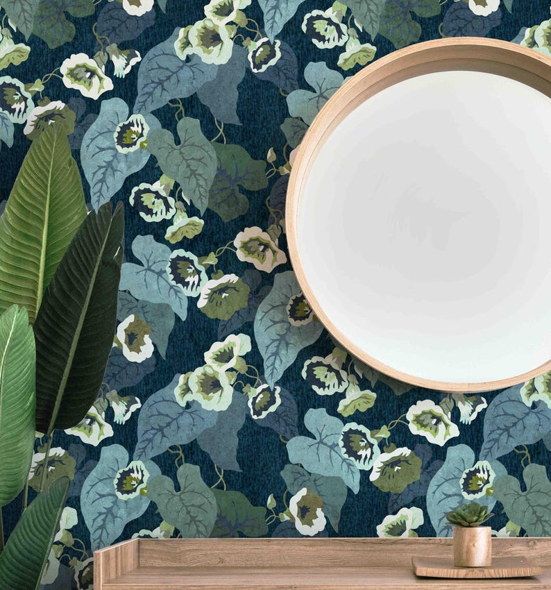 May include: A dark blue wallpaper with a repeating pattern of green leaves and white flowers. The wallpaper is shown on a wall with a round mirror and a small potted plant on a wooden shelf.