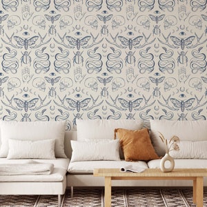 Op de afbeelding: Een witte bank met twee kussens en een salontafel ervoor. De muur achter de bank is bedekt met behang met een herhalend patroon van blauwe motten, slangen, schedels en andere symbolen.