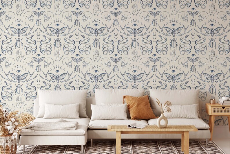 Op de afbeelding: Een witte bank met twee kussens en een salontafel ervoor. De muur achter de bank is bedekt met behang met een herhalend patroon van blauwe motten, slangen, schedels en andere symbolen.