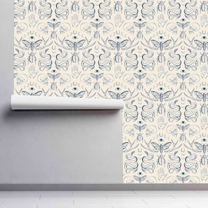 Op de afbeelding: Een cr&egrave;mekleurige behang met een herhalend patroon van blauwe illustraties. Het patroon omvat motten, slangen, handen, schedels en kevers.