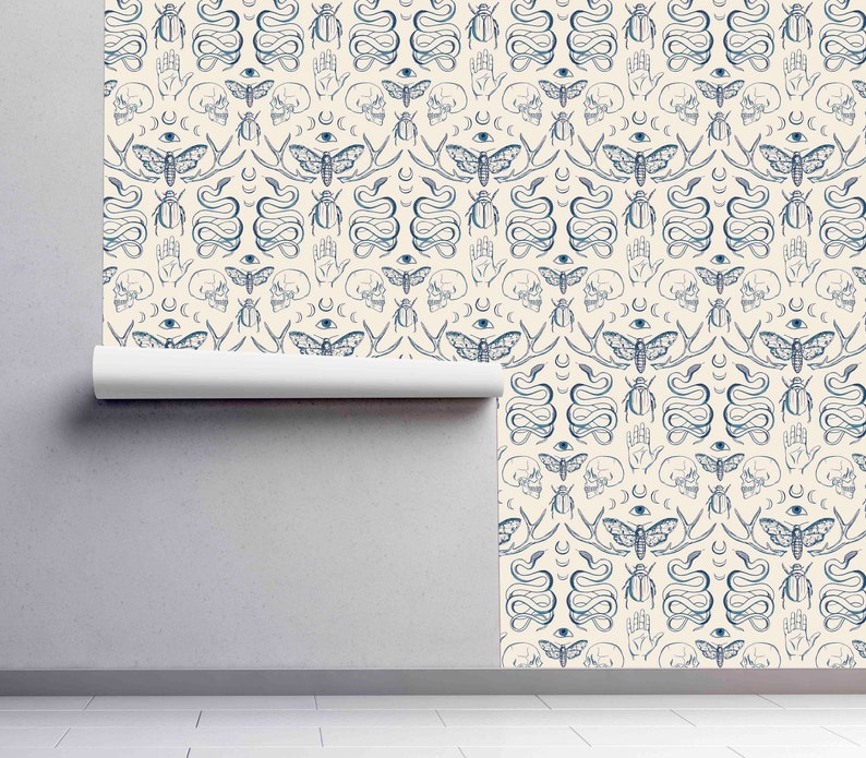 Op de afbeelding: Een cr&egrave;mekleurige behang met een herhalend patroon van blauwe illustraties. Het patroon omvat motten, slangen, handen, schedels en kevers.