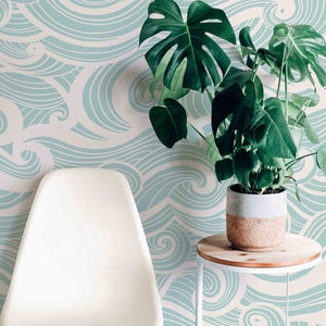 May include: A white chair with wooden legs sits in front of a wall with a blue and white wave pattern wallpaper. A potted plant with large green leaves sits on a white side table.