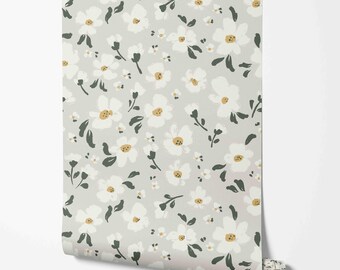 May include: A roll of wallpaper featuring a repeating floral pattern. The design includes white flowers with yellow centers and dark green leaves on a light gray background. The wallpaper is rolled up, showing the pattern's edge.