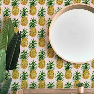 May include: A pink wall covered in a repeating pattern of yellow and green watercolor pineapples. A round, wooden-framed mirror is on the right. Large green leaves are on the left, and a wooden shelf with a small plant is at the bottom.