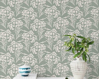 May include: A green wallpaper with a white floral pattern. A white shelf with a white vase with a green plant and a white ceramic container on top of a stack of books.