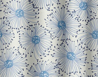 May include: Off-white fabric featuring a repeating pattern of blue floral motifs. Each flower has a central blue circle, radiating lines, and small dark blue dots, creating a delicate, airy design.