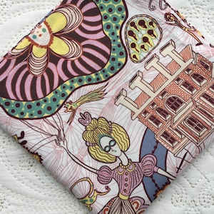 May include: A folded square fabric with a colorful, whimsical print. The design features a woman in a pink dress, a building, and abstract floral and geometric shapes in shades of pink, yellow, brown, and teal on a white background.