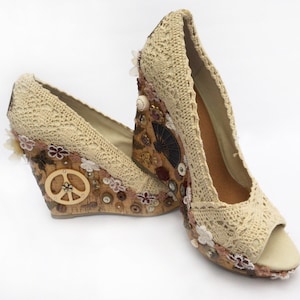 Op de afbeelding: Een paar beige gehaakte wedges met een kurken wig die versierd is met knopen, bloemen en een vredesteken.