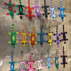 May include: A collection of beaded lizard keychains in various colors, including green, red, orange, purple, blue, and black. Each lizard has a keyring attached. The lizards are made of small, colorful beads.