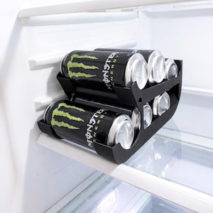 May include: A black can organizer holding energy drink cans inside a refrigerator. The cans are black with a green claw design and the word "Monster" in white. The organizer is on a shelf.