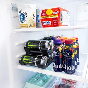 May include: A refrigerator interior with various food items. Includes yogurt, Lactaid milk, energy drinks, and protein shakes. The energy drinks are black with green accents, and the protein shakes are in dark blue bottles with fruit graphics.