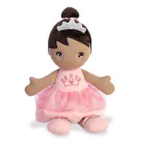 May include: A brown-skinned plush doll wearing a pink ballerina dress with a crown and a heart on the front. The doll has brown hair and a silver tiara.
