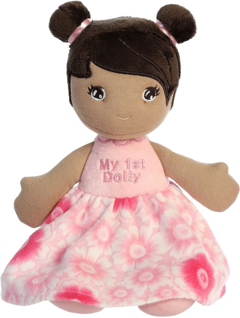 May include: A plush doll with brown hair, brown eyes, and a pink dress with white flowers. The dress has the text "My 1st Dolly" embroidered on the front.
