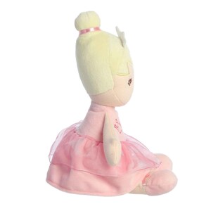 May include: A plush ballerina doll with blonde hair, wearing a pink tutu and a crown. The doll has a sweet, embroidered face and the words "Rise & Shine" on its chest.