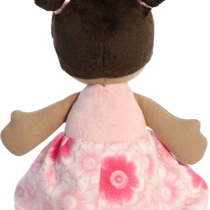 May include: A plush doll with brown hair in pigtails wearing a pink dress with a floral pattern.