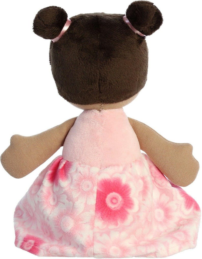 May include: A plush doll with brown hair in pigtails wearing a pink dress with a floral pattern.