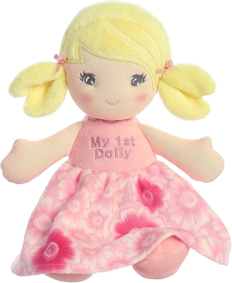 May include: A pink and white plush doll with yellow hair in pigtails. The doll is wearing a pink dress with a floral pattern and has the words "My 1st Dolly" embroidered on the front.
