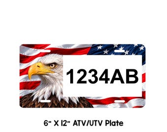 May include: A rectangular 6 inch by 12 inch ATV/UTV license plate featuring a graphic of a bald eagle head on the left side and a waving American flag background. A white rectangular box on the right displays the black alphanumeric text 1234AB.