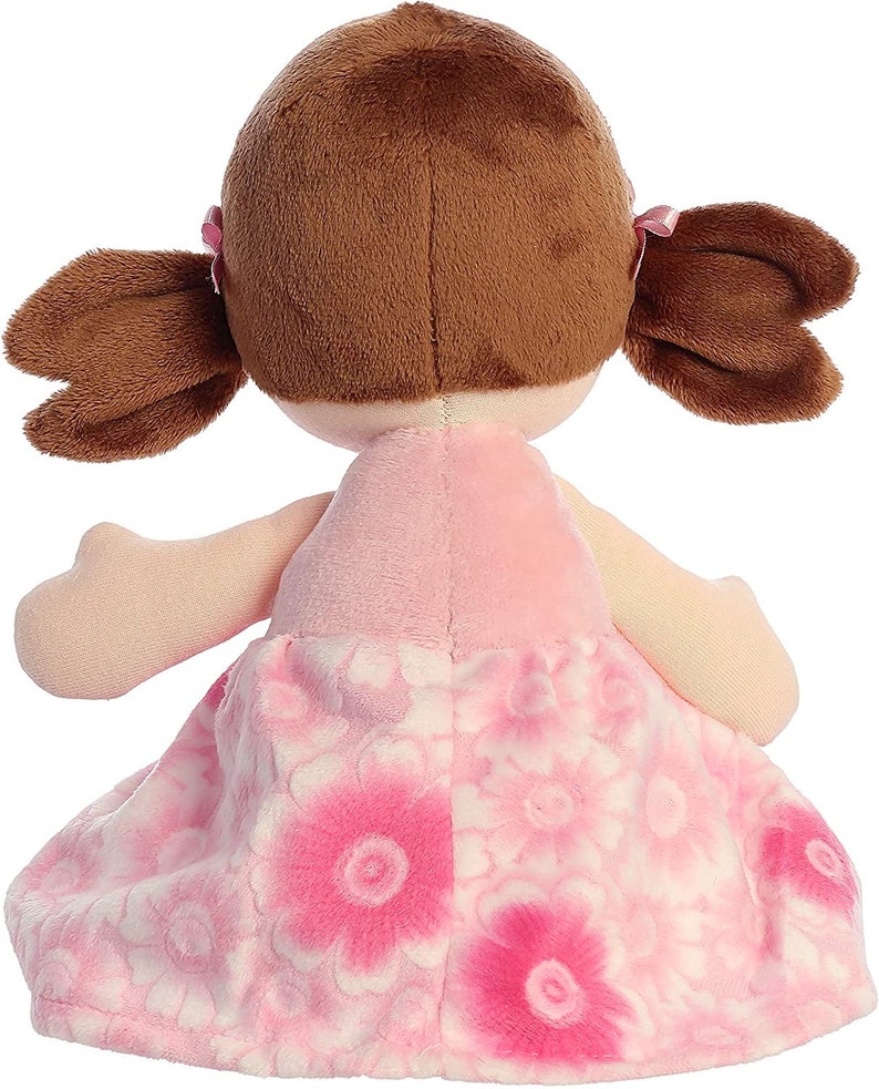 May include: A pink plush doll with brown hair in pigtails wearing a pink dress with white flowers.