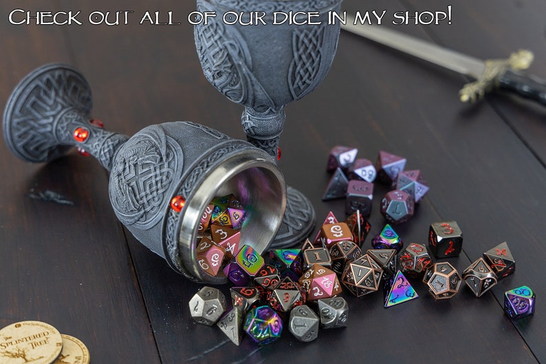 May include: A collection of metal dice in various colors, including iridescent, black, and red, spilling out of a silver chalice with a gray, ornate design. The chalice is resting on a wooden surface.