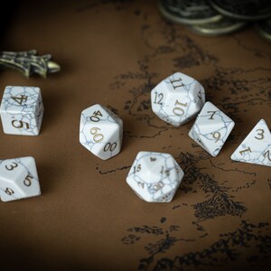 May include: A set of six white dice with gold numbers on a brown background. The dice are in various shapes and sizes, including a d4, d6, d8, d10, d12, and a d20.
