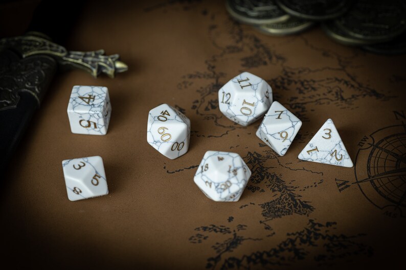 May include: A set of six white dice with gold numbers on a brown background. The dice are in various shapes and sizes, including a d4, d6, d8, d10, d12, and a d20.