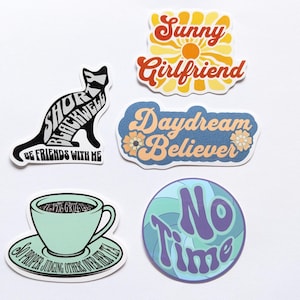 Puede incluir: Cinco pegatinas coloridas con varios diseños y textos. Las pegatinas incluyen un gato negro con el texto "Short Blackwel Be Friends With Me", un sol amarillo con el texto "Sunny Girlfriend", una flor azul y blanca con el texto "Daydream Believer", un remolino azul y verde con el texto "No Time", y una taza de té verde con el texto "So Proper Judging Others Other Than Me".