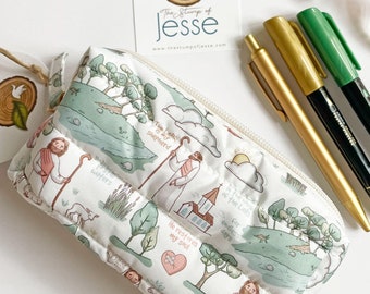 May include: A white zippered pouch with a quilted design featuring a repeating pattern of a shepherd with sheep, a church, and the words "The house of the Lord", "He restores my soul", "For endless days", and "The Lord is my shepherd".