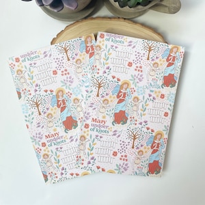May include: Two pink and white patterned cards with the text "Mary undoer of knots" and "undoer of knots". The cards feature a repeating pattern of flowers, trees, and angels.