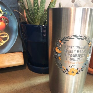 Op de afbeelding: Een roestvrijstalen tumbler met een bloemensticker met een citaat van Theresia van Lisieux: "Als elke kleine bloem een roos wilde zijn, zou de lente zijn schoonheid verliezen."