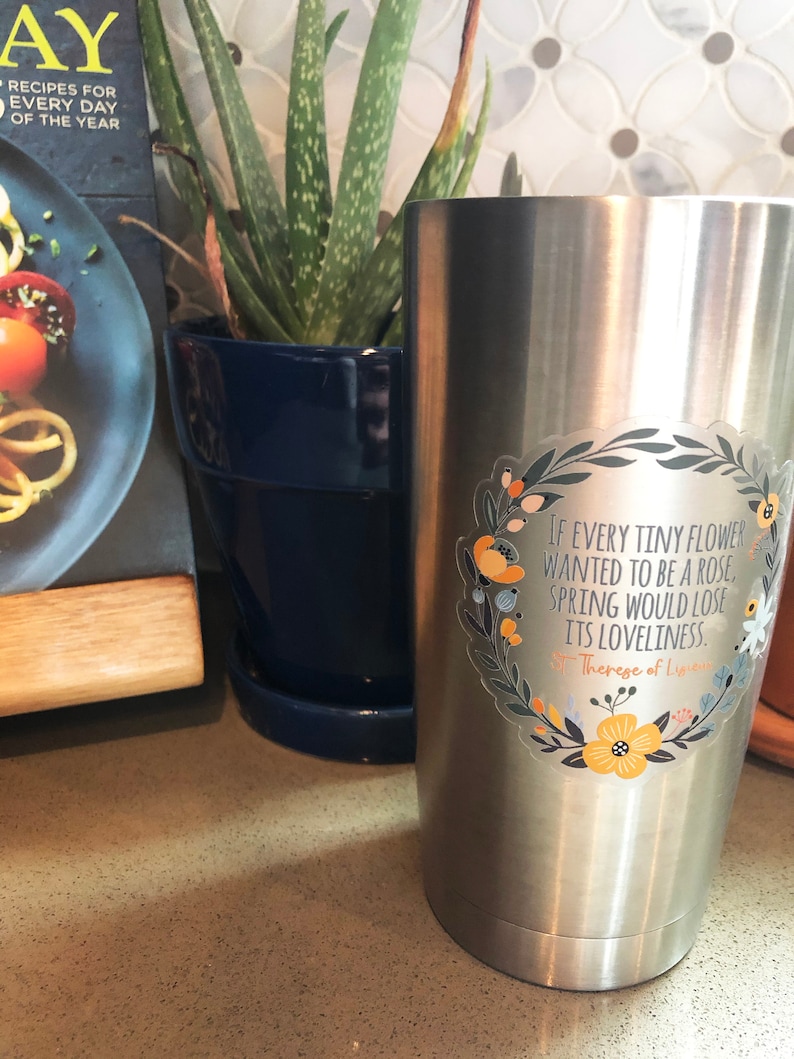 Op de afbeelding: Een roestvrijstalen tumbler met een bloemensticker met een citaat van Theresia van Lisieux: "Als elke kleine bloem een roos wilde zijn, zou de lente zijn schoonheid verliezen."