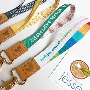 May include: Four fabric lanyards with gold-tone metal lobster clasps and tan leather accents embossed with a bird logo. The lanyards feature various patterns and text including "CARE OF EVERYTHING", "AM YOUR MOTHER?", and "love joy peace patience".