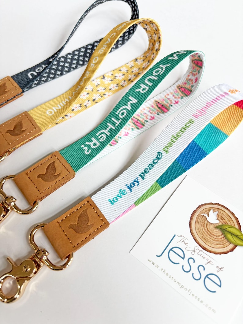 May include: Four fabric lanyards with gold-tone metal lobster clasps and tan leather accents embossed with a bird logo. The lanyards feature various patterns and text including "CARE OF EVERYTHING", "AM YOUR MOTHER?", and "love joy peace patience".