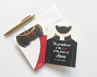 May include: Greeting cards with religious illustrations. One card has the quote: "The priesthood is the love of the heart of Jesus." A gold pen and a white envelope are also in the image.