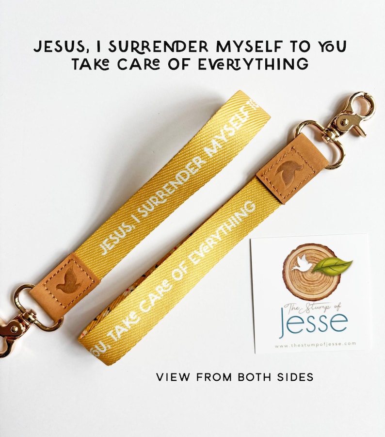 May include: A yellow fabric wristlet keychain featuring the white text "JESUS, I SURRENDER MYSELF TO YOU" and "TAKE CARE OF EVERYTHING". It includes a tan leather accent piece embossed with a dove and a gold-toned metal lobster clasp.